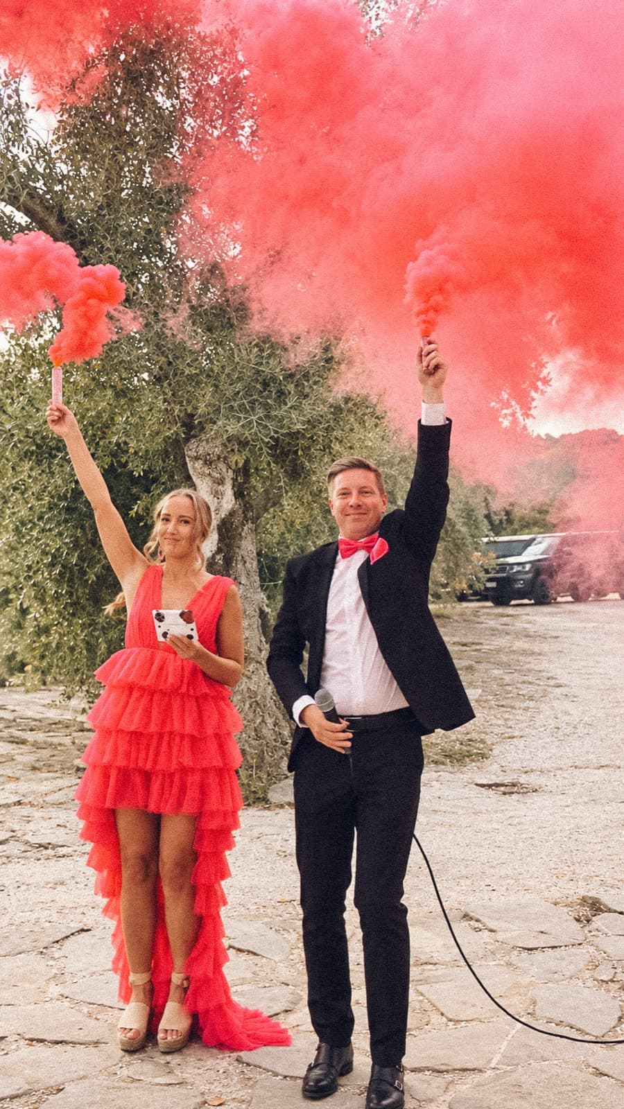Toastmaster och gäst håller upp röda rökbomber vid ett bröllop bland olivträd i Italien