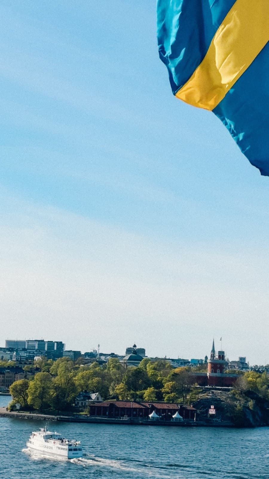 Svenska flaggan i vinden med utsikt över Stockholm och vattnet